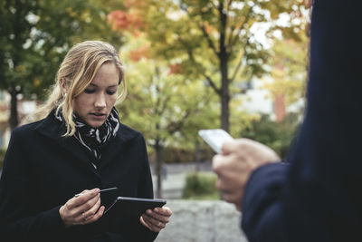 Mid adult businesswoman using smart phone with man in foreground outdoors