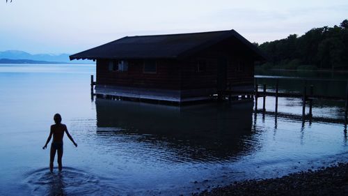 Silhouette girl standing in lake by house against sky