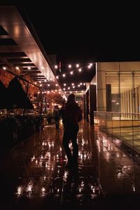 Rear view of man walking on illuminated street at night