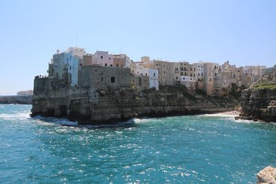 Buildings by sea against clear blue sky