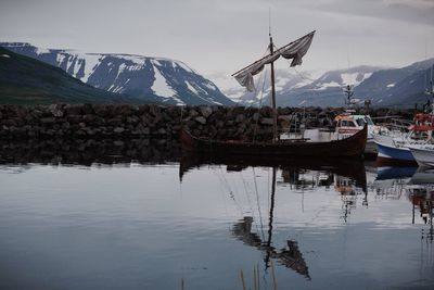 Sailboats moored in lake by snowcapped mountains against sky