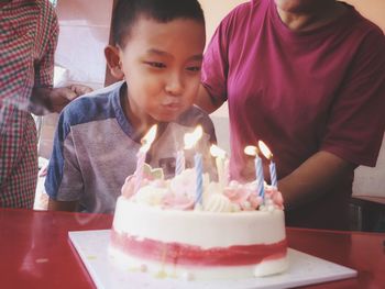 Boy blowing birthday candles on cake with family at home