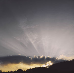 Low angle view of sunlight streaming through clouds during sunset