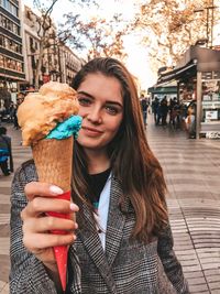 Portrait of young woman holding ice cream cone while standing on city street