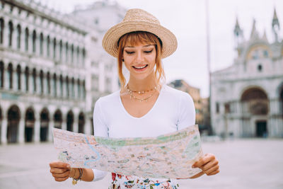 Smiling woman holding map standing against building