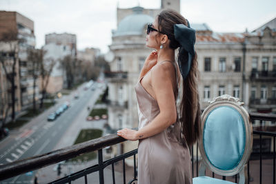 Side view of young woman standing on railing in city