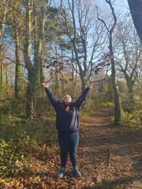 Woman throwing leaves while standing in forest