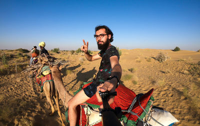 Portrait of young man riding on camel at desert against clear sky