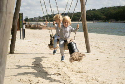 Cute boys sitting on swing at beach