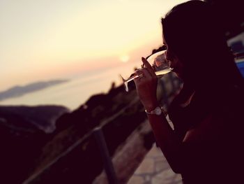 Woman drinking wine against sea during sunset