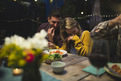 Happy couple sitting at table while enjoying dinner party with friends
