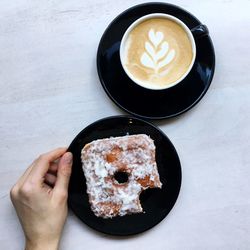 Cropped hand holding plate with donut by coffee cup on table