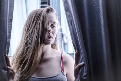 Young woman standing amidst curtain at home