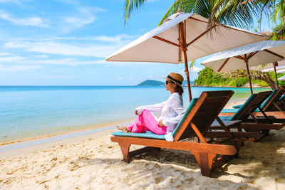 Rear view of woman sitting on beach against sky