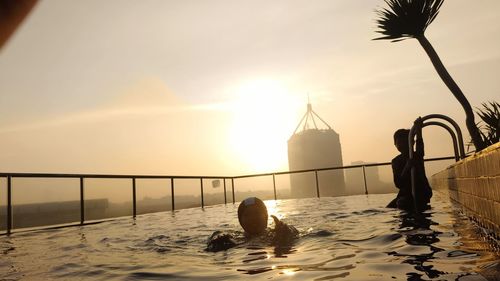 Low section of woman standing in sea against sky during sunset