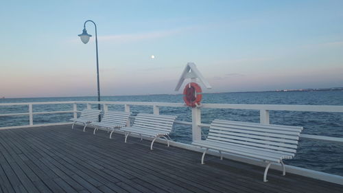 Empty bench on pier by sea against sky
