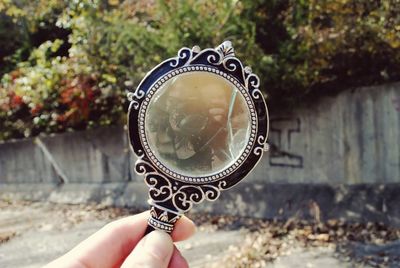 Cropped image of woman holding mirror against retaining wall