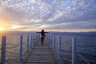 Rear view of woman walking on pier over sea against cloudy sky