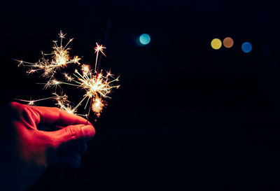 Cropped hand of person holding illuminated sparkler at night