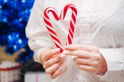 Midsection of woman holding candy canes at home during christmas