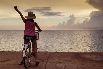 Man riding bicycle on beach against sky during sunset
