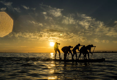 Silhouette people paddleboarding on sea against sky during sunset