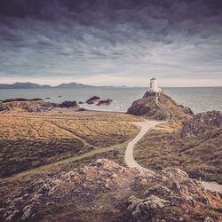 Lighthouse at ynys llanddwyn by sea against cloudy sky