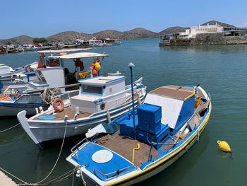 Fishing boats moored at harbor against blue sky