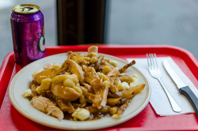 High angle view of chicken poutine served in plate with drinking can on tray