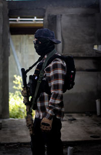 Young man holding rifle wearing mask standing in corridor