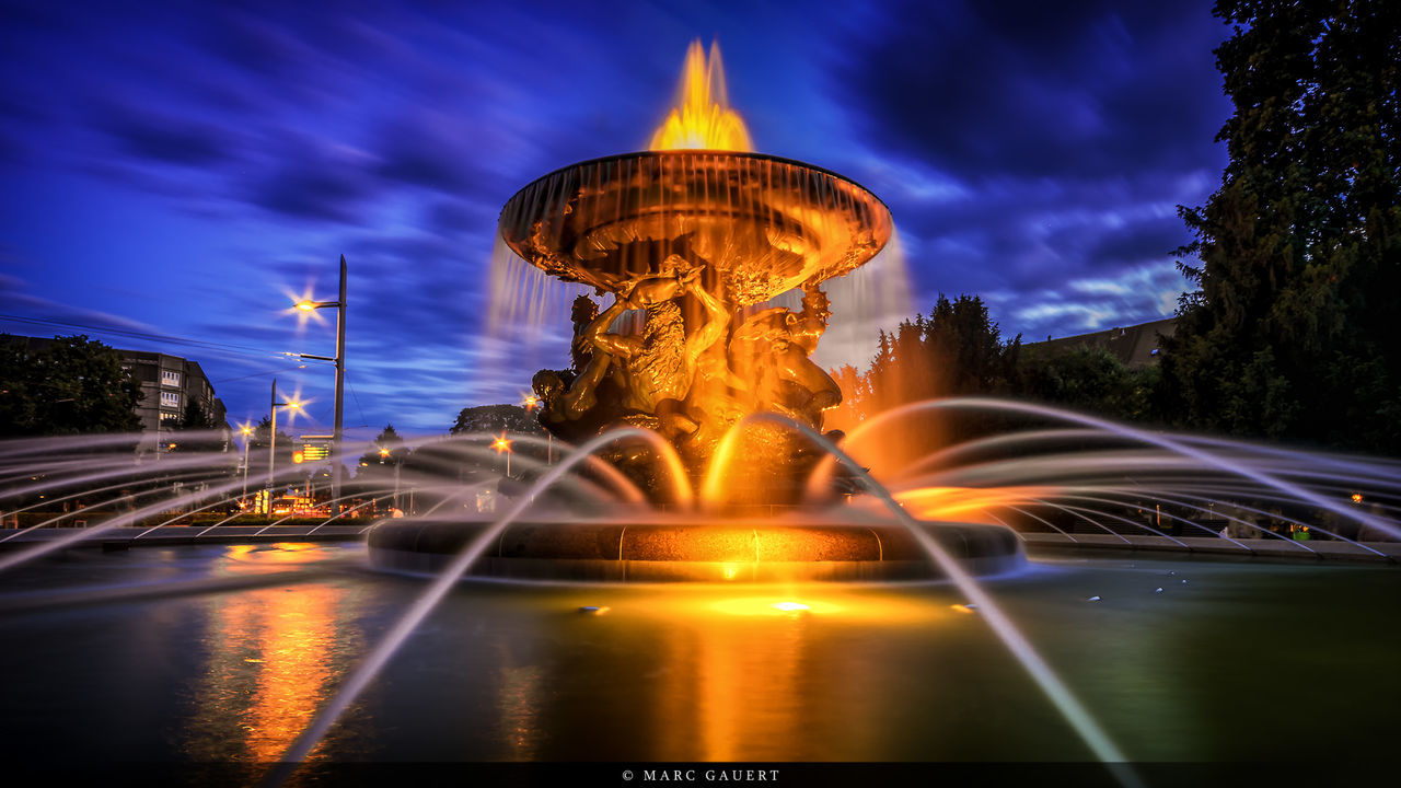 illuminated, long exposure, night, sky, light trail, motion, transportation, blurred motion, built structure, architecture, speed, cloud - sky, reflection, water, travel destinations, dusk, travel, city, blue, building exterior