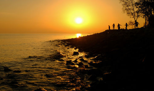 Silhouette people on beach against sky during sunset