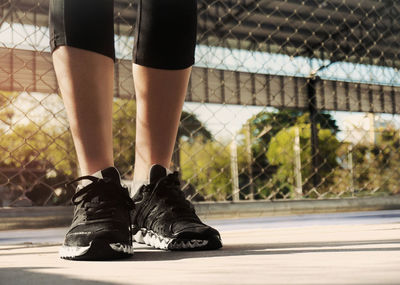 Low section of woman wearing black sports shoes while standing against fence