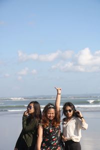 Woman gesturing while standing with friends at beach against sky