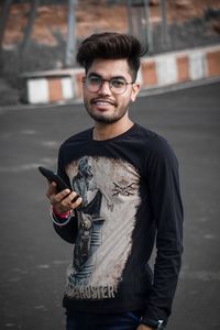 Portrait of young man holding smart phone while standing on road