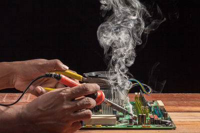 Close-up of man welding motherboard on table against black background
