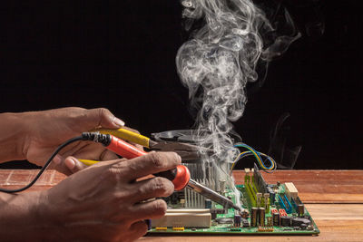 Midsection of person holding cigarette at table against black background