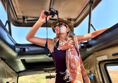 Woman holding binoculars while peeking from car sunroof