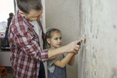 Father and daughter standing against wall at home