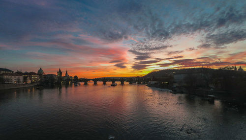 Scenic view of river by buildings against sky during sunset