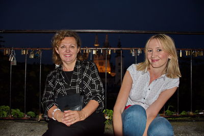 Two mature women sitting by the fence with cityscape of zagreb against night background