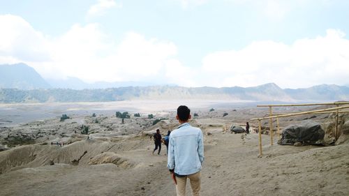 Rear view of man standing on mountain against sky