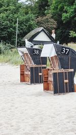 Hooded chairs on beach by house against trees