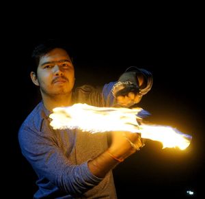 Young man holding lit candle against black background