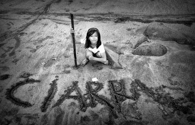 High angle portrait of girl crouching by ciarra text at beach