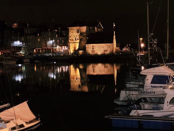 Sailboats moored in harbor against buildings at night