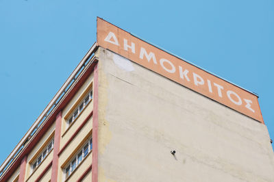 Low angle view of text on building against clear blue sky