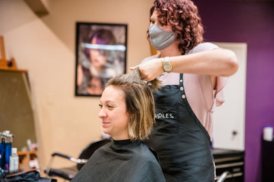 Hairdresser wearing flu mask dyeing hair of client in salon