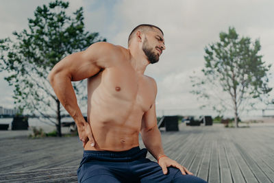 Shirtless man with backache sitting outdoors