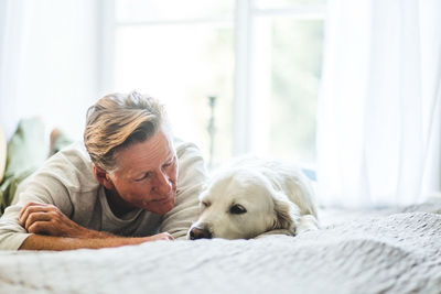 Close-up of senior man looking at cute dog while lying on bed in bedroom